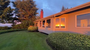 Una casa moderna amb una xemeneia gran, un jardí ben cuidat i vistes al capvespre.