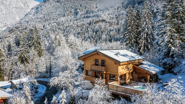 A wooden cabin with a balcony, surrounded by snow-covered trees and mountains in the background. - Chalet Choquette - secluded family break for 7 with spa - OVO Network (Les Houches)