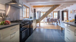 A modern kitchen with a central island, stainless steel appliances, and a wooden staircase leading to a dining area. - Chalet Choquette - secluded family break for 7 with spa - OVO Network (Les Houches)