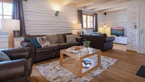 A cozy living room with a brown leather sofa, a wooden coffee table, and a television in the background. - Chalet Choquette - secluded family break for 7 with spa - OVO Network (Les Houches)