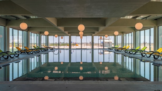 Une piscine dotée de chaises longues et de grandes fenêtres.