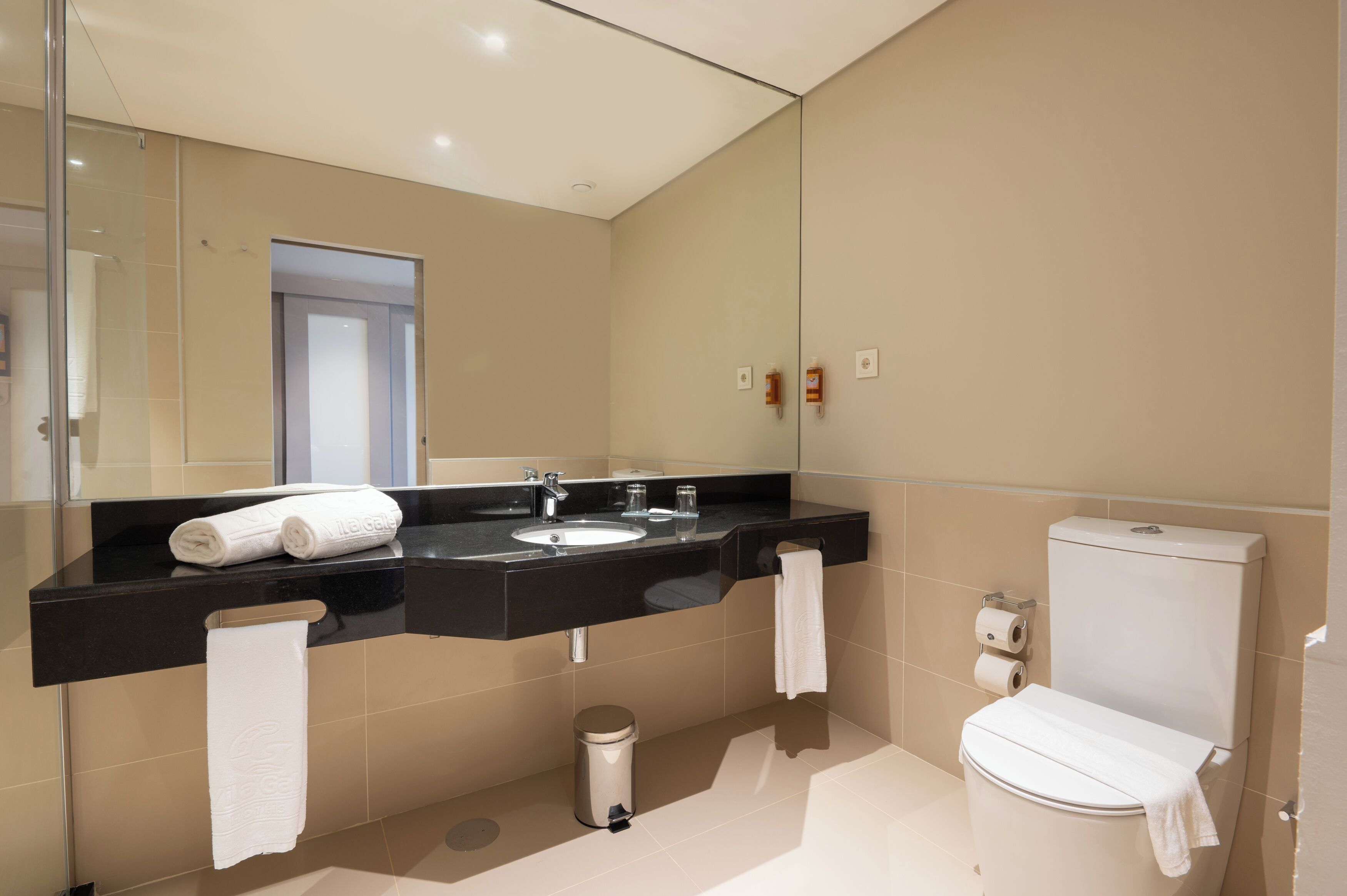 A modern bathroom with a black countertop sink, a mirror, a toilet, and a trash can.