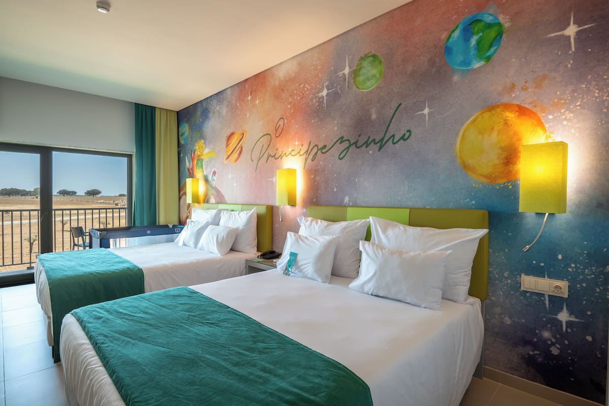 A hotel room with two beds, a large window, and a mural of planets on the wall.