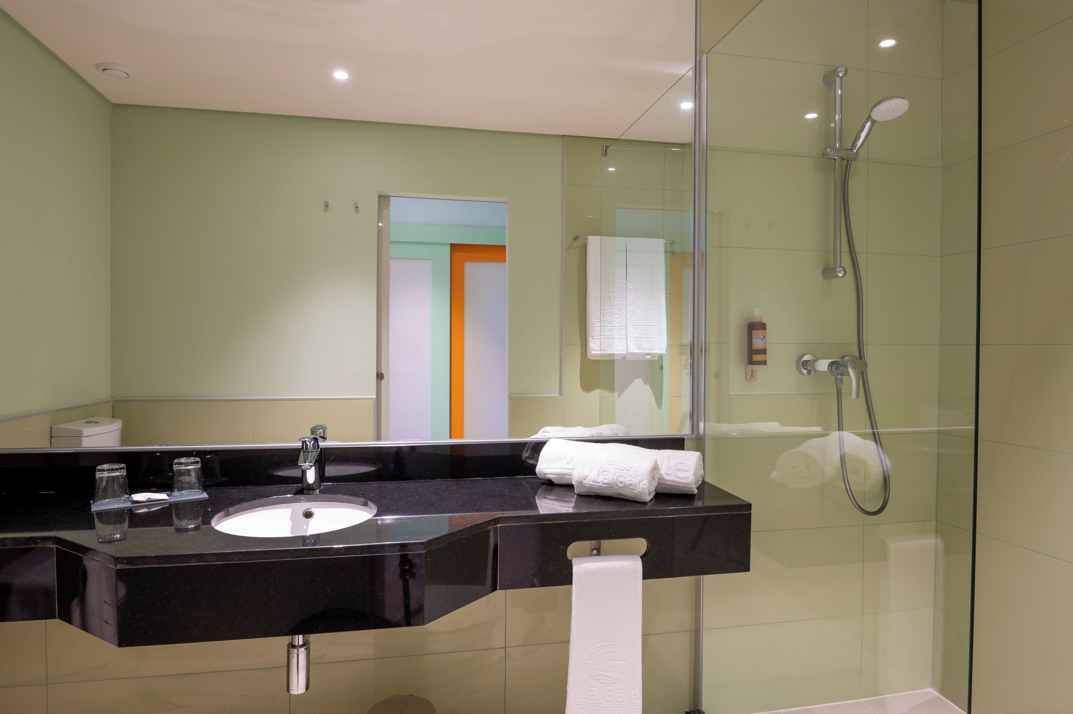 A modern bathroom with a black sink, glass shower enclosure, and a mirror reflecting a door with orange and white panels.