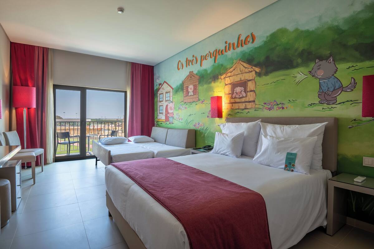 A hotel room with two beds, a large window, and a mural on the wall.