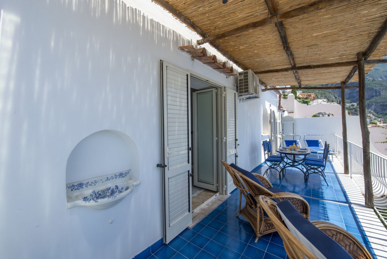 Un espace extérieur abrité, doté d’une table et de chaises, d’une porte et offrant une vue sur un paysage montagneux.
