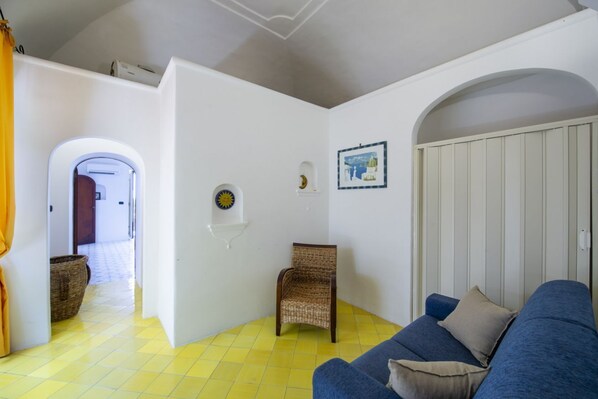 A room with a blue sofa, a wicker chair, and a yellow tiled floor.