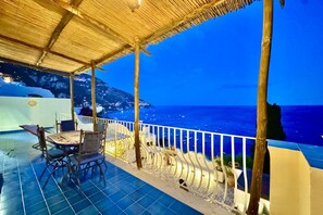 A terrace with a table and chairs, overlooking a coastal view.