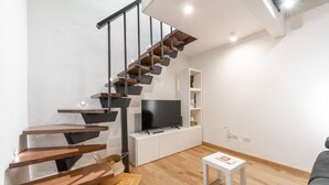 A modern living room with a wooden staircase, a flat-screen TV, white cabinetry, and a grey sofa. - Modern Gem in Castello (Cagliari)