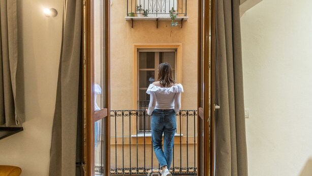 A person walking through a doorway into a room with a window and a balcony with plants. - Modern Gem in Castello (Cagliari)