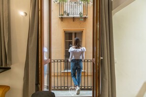 A person walking through a doorway into a room with a window and a balcony with plants.