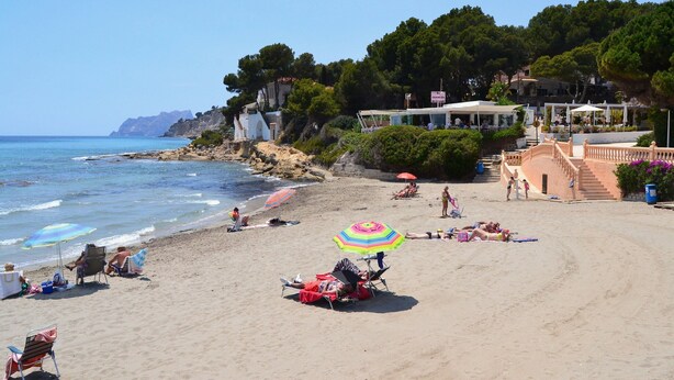 A beach with people sunbathing, umbrellas, and a staircase leading to a building. - Villa beach (VC)