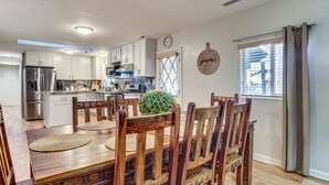 Een ruime keuken met witte kasten, roestvrijstalen apparatuur en een houten eettafel met stoelen.