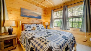 Een houten slaapkamer met een groot bed, twee bedlampen, een schilderij aan de muur en een raam met gordijnen.