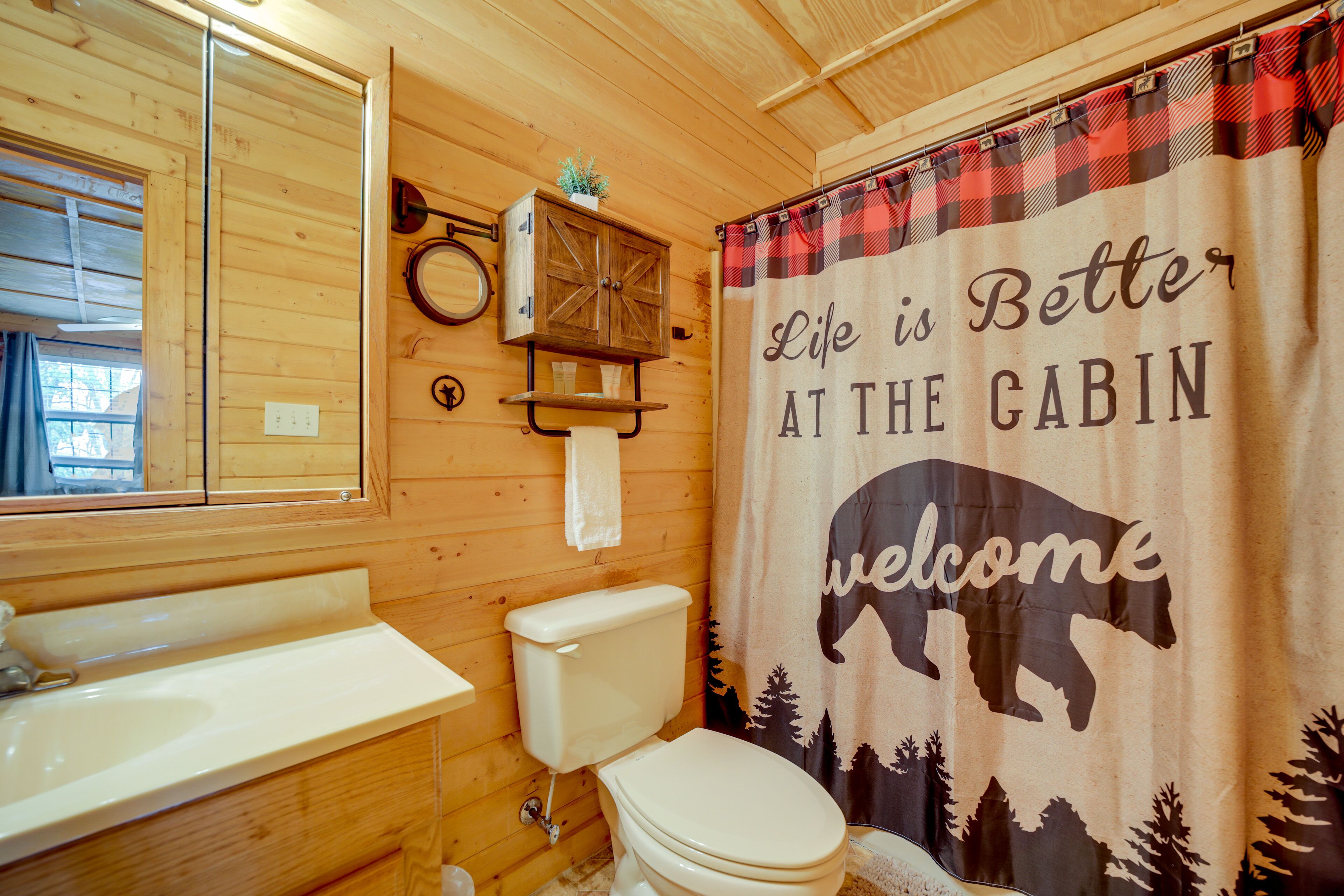 Ein Badezimmer in einer Holzhütte mit Toilette, Waschbecken und einer Duschkabine mit freundlicher Willkommensbotschaft.
