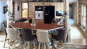 A rustic cabin interior with a wooden dining table, chairs, and a kitchen area. - The Wyoming Lodge and Game Room (Dubois)