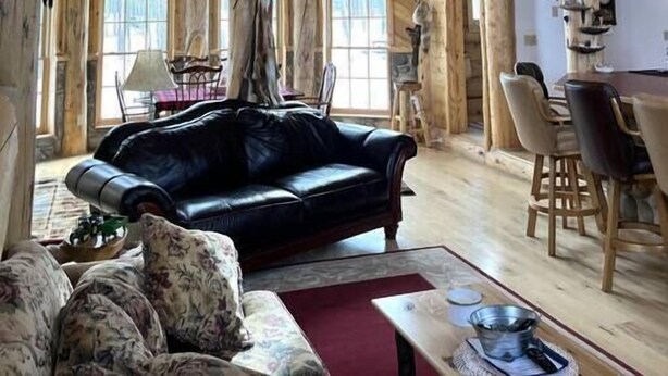A rustic cabin interior with a black leather sofa, a dining area, and wooden walls adorned with deer antlers. - The Wyoming Lodge and Game Room (Dubois)