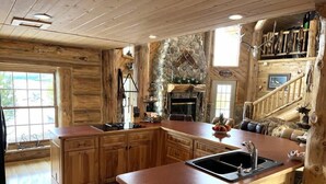 A rustic cabin-style kitchen with wooden cabinetry, a stone fireplace, and a dining area with a large island. - The Wyoming Lodge and Game Room (Dubois)