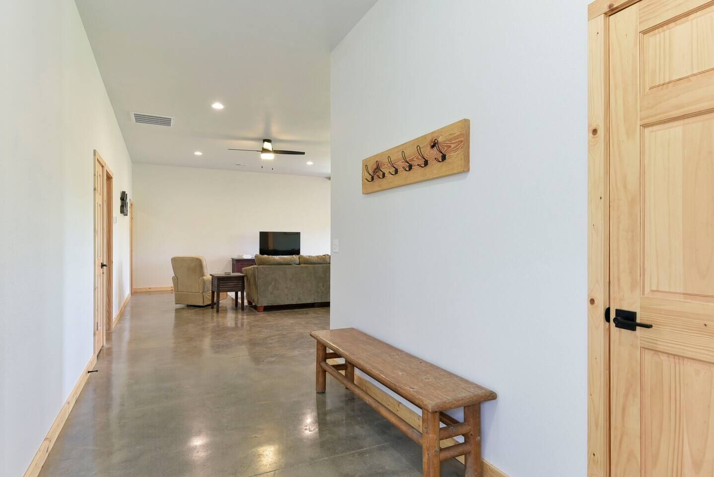 A hallway with a wooden bench, a sofa, a television, and a wall-mounted artwork.