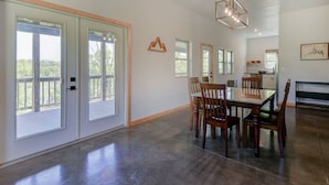 A spacious dining area with a large table and chairs, a kitchen in the background, and a balcony with a view. - Lakefront Retreat w/Views, Fire Pit & 2 Acres (Golden)