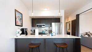 A modern kitchen with a central island, bar stools, a microwave, and a refrigerator.