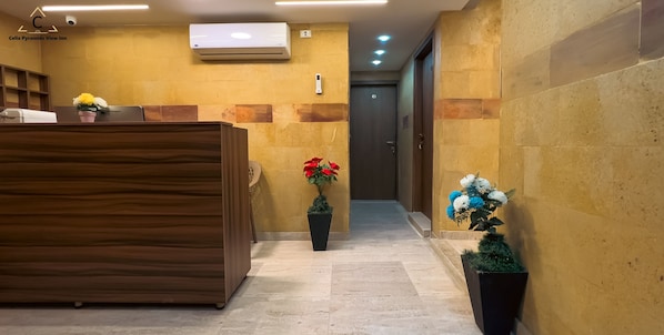 A reception desk with a wooden finish, a potted plant with red flowers, and a wall-mounted air conditioner. - Celia Pyramids View inn (Giza)