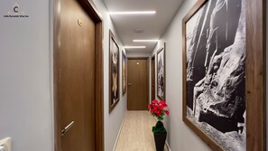 Un couloir avec des portes en bois, des œuvres d’art encadrées et une plante en pot ornée de fleurs rouges.