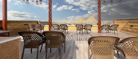 A rooftop terrace with wicker chairs and tables, offering a view of the pyramids.