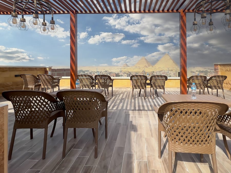 Terraza en la azotea con sillas y mesas de mimbre, con vistas a las pirámides.