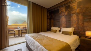 Une chambre d’hôtel avec un grand lit, une petite table avec des chaises et une vue sur les pyramides.