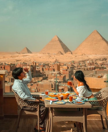 A dining table with plates of food and drinks, overlooking a cityscape with pyramids in the background.