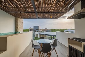 A modern outdoor patio with a glass table and chairs, a wooden ceiling, and a view of buildings in the distance.