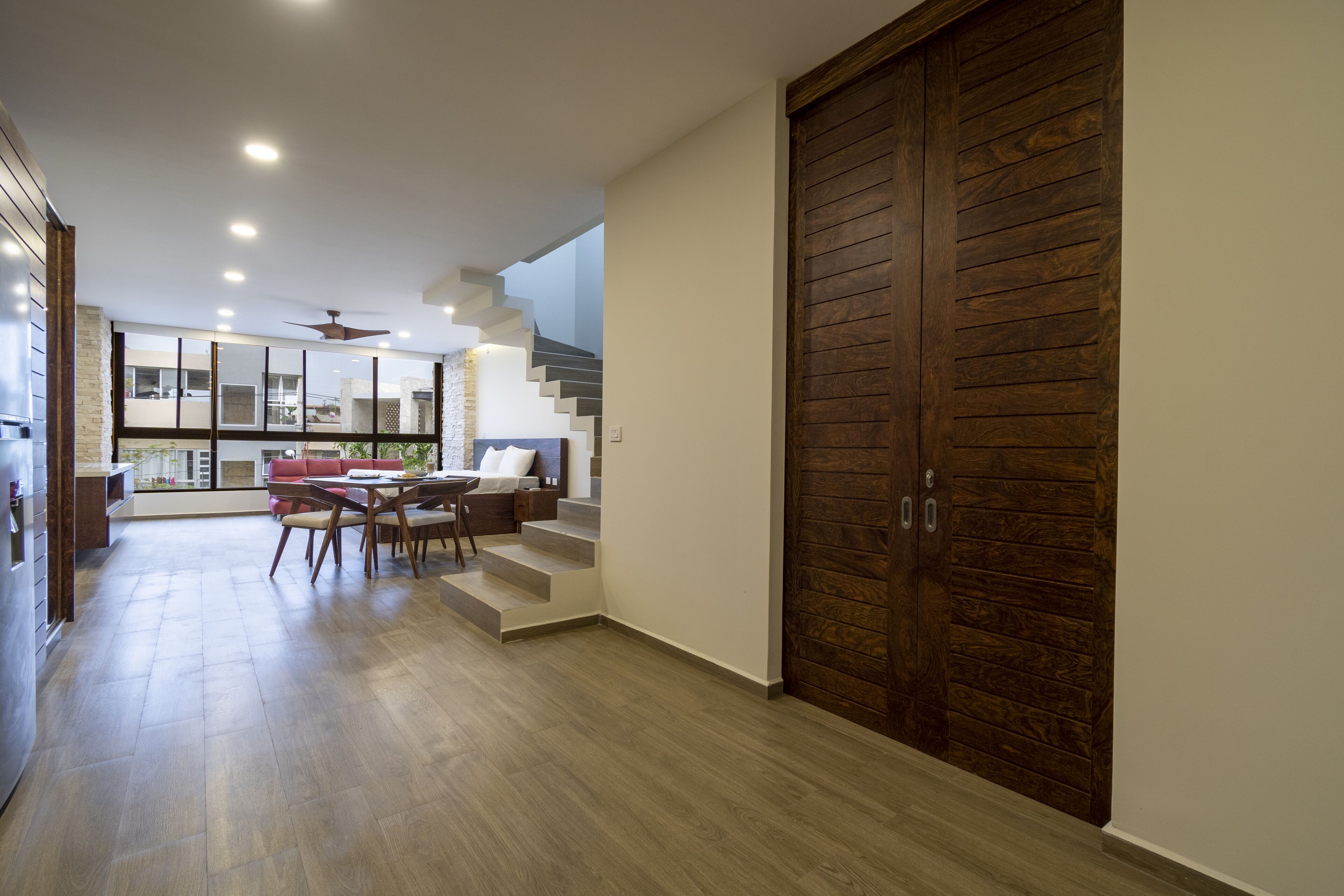 A modern interior with a wooden door, a staircase, and a dining area with a table and chairs.