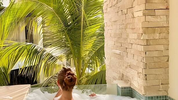 A person in a hot tub surrounded by palm trees and a stone wall. - Moots Tulum (Tulum)