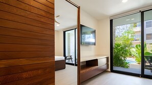 A modern living room with a large TV, wooden panel wall, and a sliding glass door leading to a balcony with greenery. - Moots Tulum (Tulum)