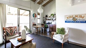 A spacious living area with a large window, a dining table, and a kitchen in the background.