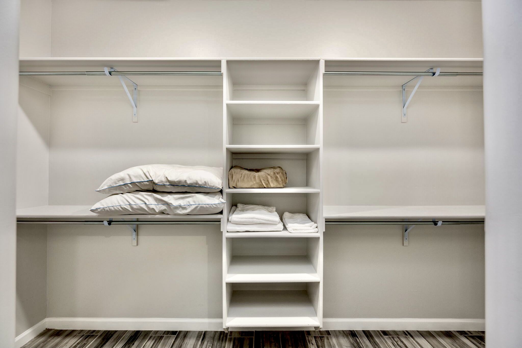 Un armario blanco con múltiples estantes y barras para colgar, que muestra ropa y almohadas ordenadas.