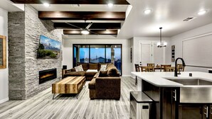A modern living room with a stone fireplace, a sectional sofa, and a large window offering a city view. - Modern Accessorized 3-Bedroom (Las Cruces)
