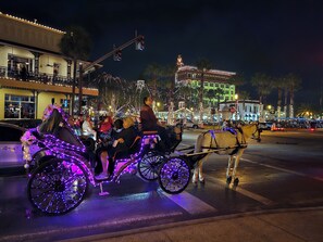 A horse-drawn carriage with illuminated wheels and a horse, pulled by a person, on a street at night.