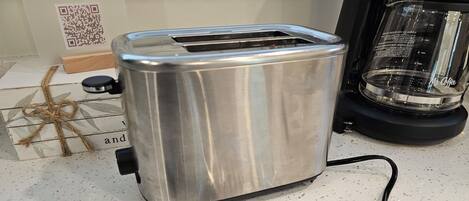 A stainless steel toaster on a kitchen counter with a QR code, a glass container, and a metal tool.