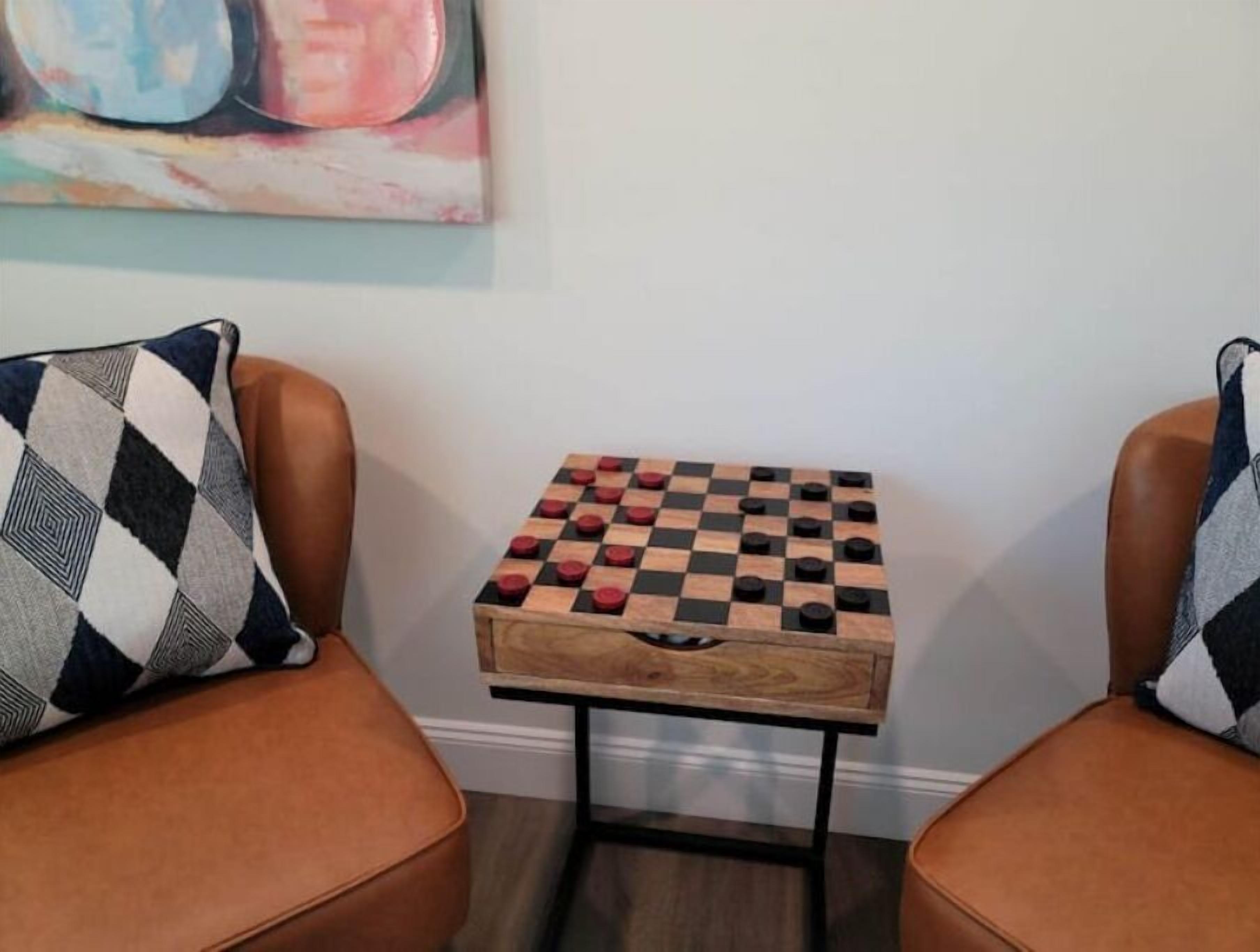 A small wooden chess table between two leather armchairs with patterned pillows.
