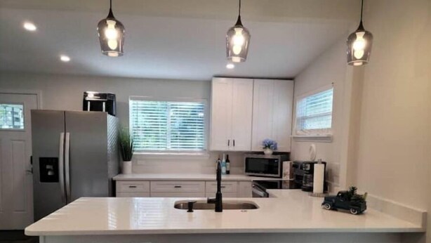 Una cucina moderna con isola centrale, due sgabelli da bar, frigorifero, forno a microonde e illuminazione a sospensione.
