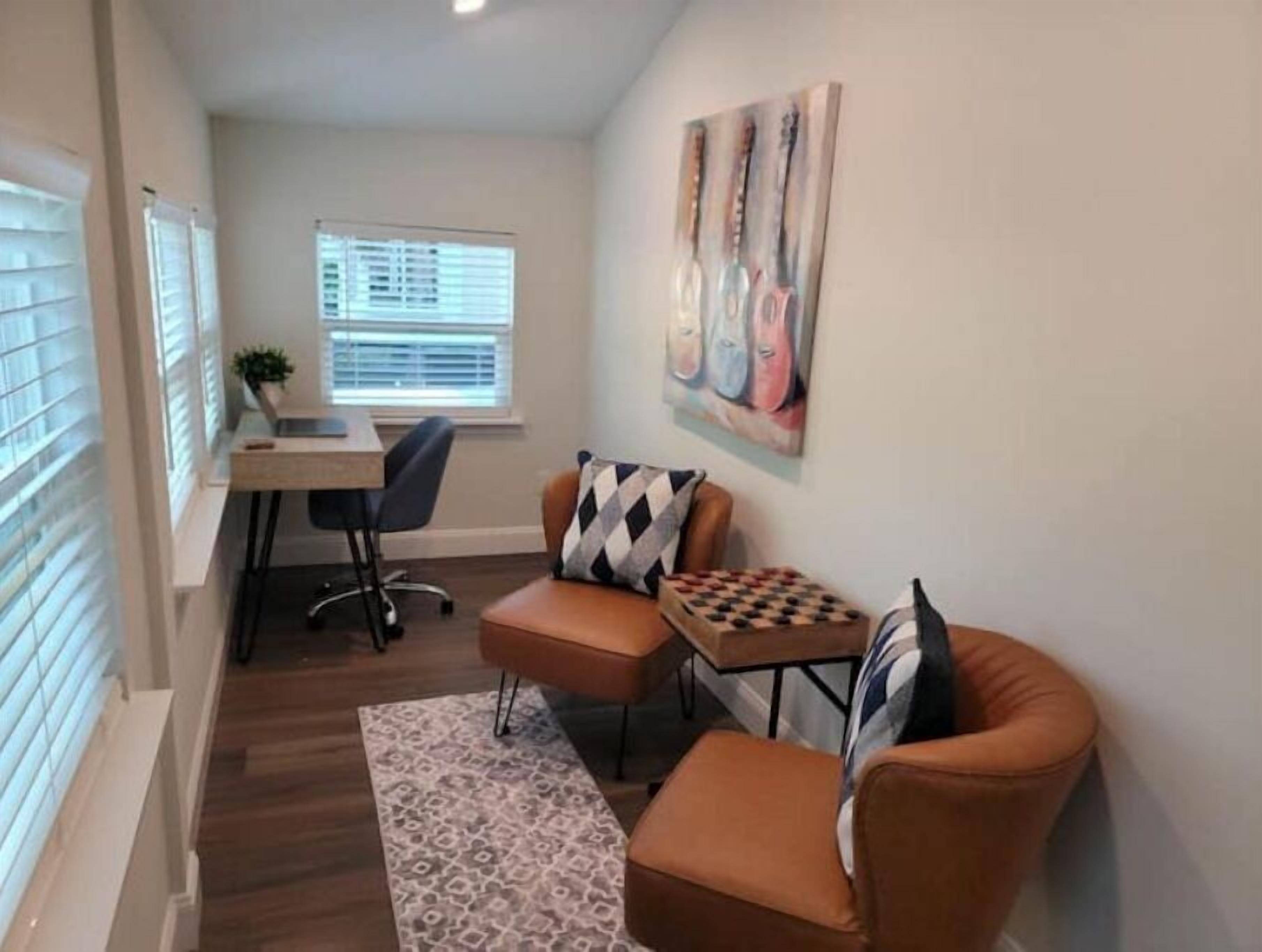 A compact living space with a desk, two chairs, a small table with a chessboard, and a painting on the wall.