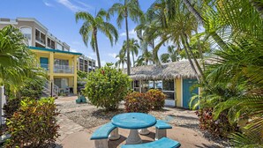 A courtyard with a round table and benches, surrounded by palm trees and a building with balconies.