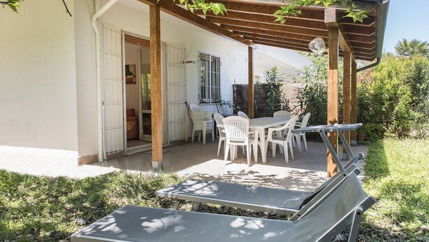 En täckt uteplats med ett bord och stolar, en pergola och två solstolar.