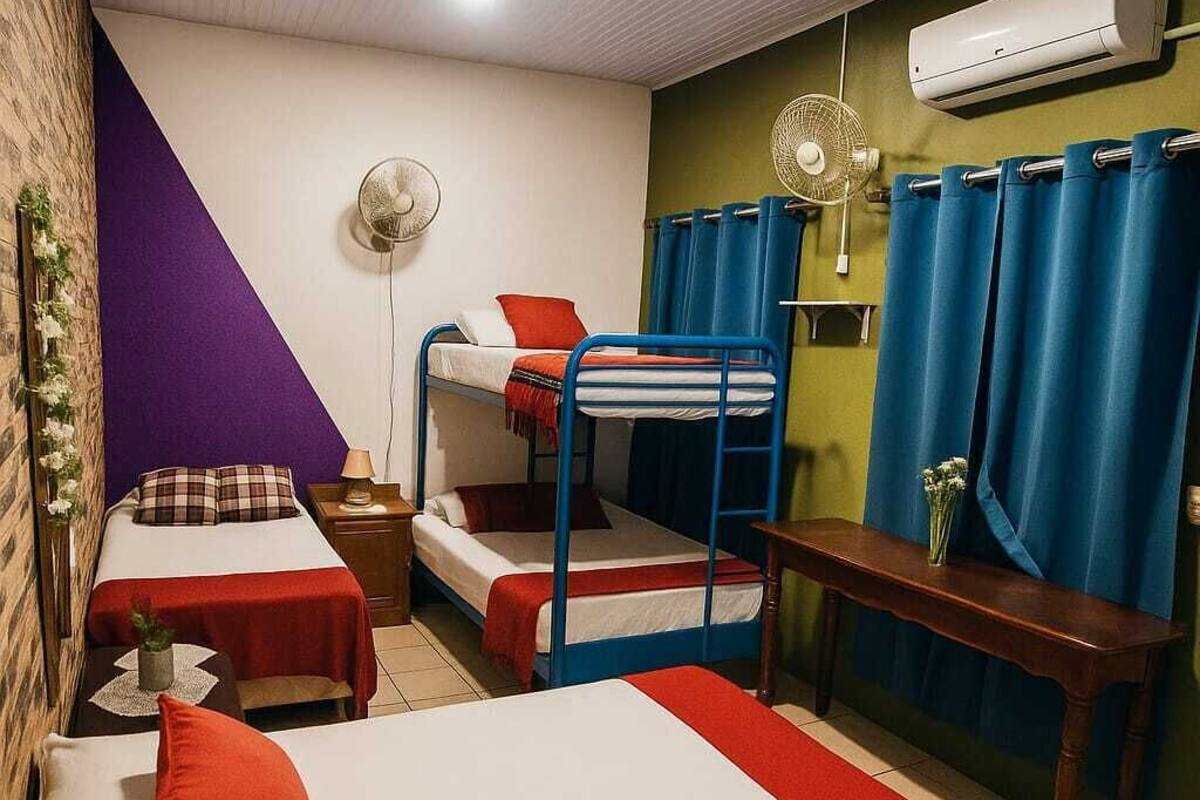 Una habitación con literas, una cama individual, una mesa y un ventilador.