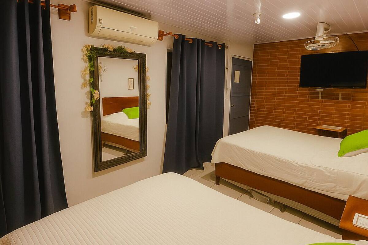 Habitación de hotel con dos camas, un espejo grande, un equipo de aire acondicionado, un televisor y un ventilador de techo.