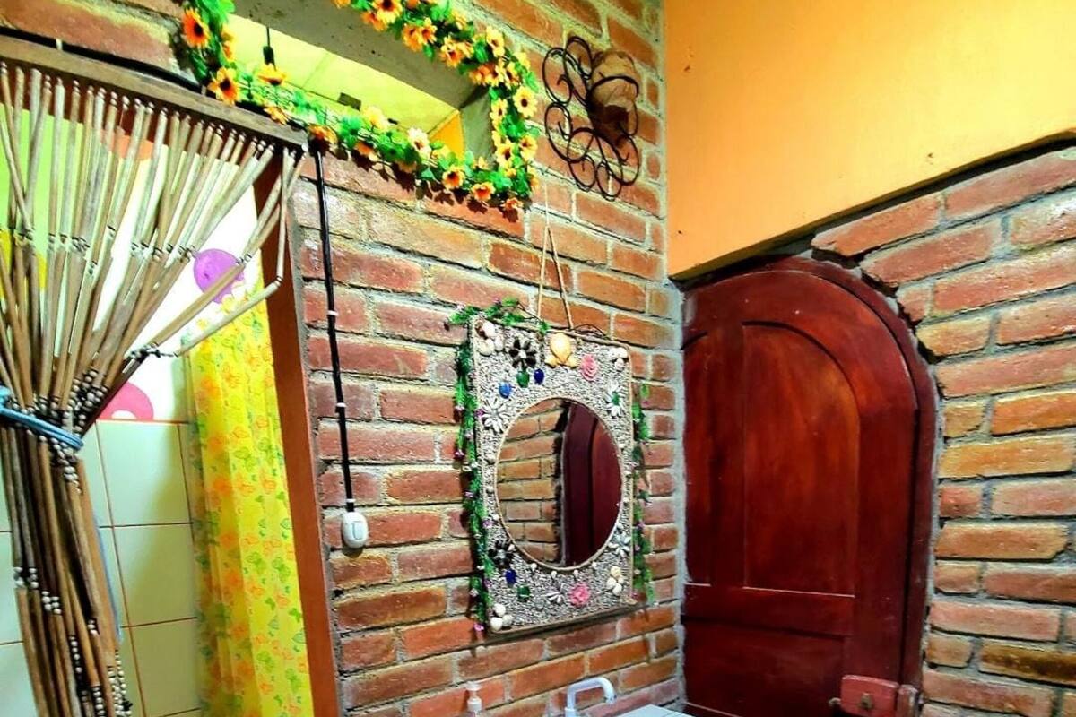 Un baño con pared de ladrillo, puerta de madera, espejo, lavabo e inodoro.