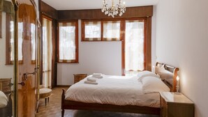 A bedroom with a wooden bed, a chandelier, a bedside table with a candle, and a window with curtains. - GuestHost - Cozy apartment of about 110 square meters, able to accommodate up to 5 people, located on the 2nd floor of a building with lift and garage.The apartment has an enchanting view of the sea and the marina, surrounded by the greenery of Villa Orm (Sanremo)