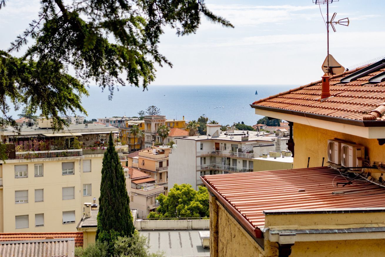 A coastal cityscape with buildings, a clear sky, and the sea in the background.